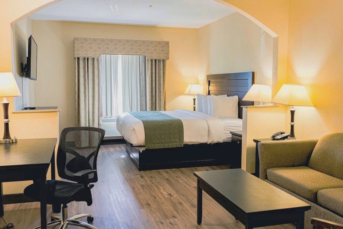 Ein Hotelzimmer mit einem Bett, zwei Nachttischlampen, einem Schreibtisch, einem Sessel und einem Sofa.