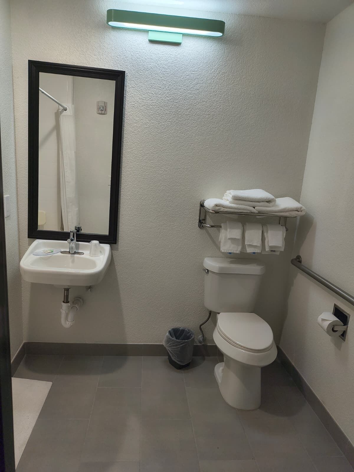 Un bagno con lavandino, specchio, water e porta asciugamani.
