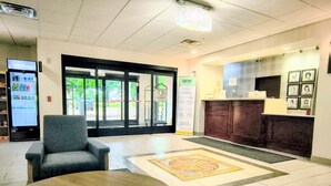 A lobby with a reception desk, a seating area, a vending machine, and a view through the glass doors. - Grander Inn & Suites by IHG (Tyler)