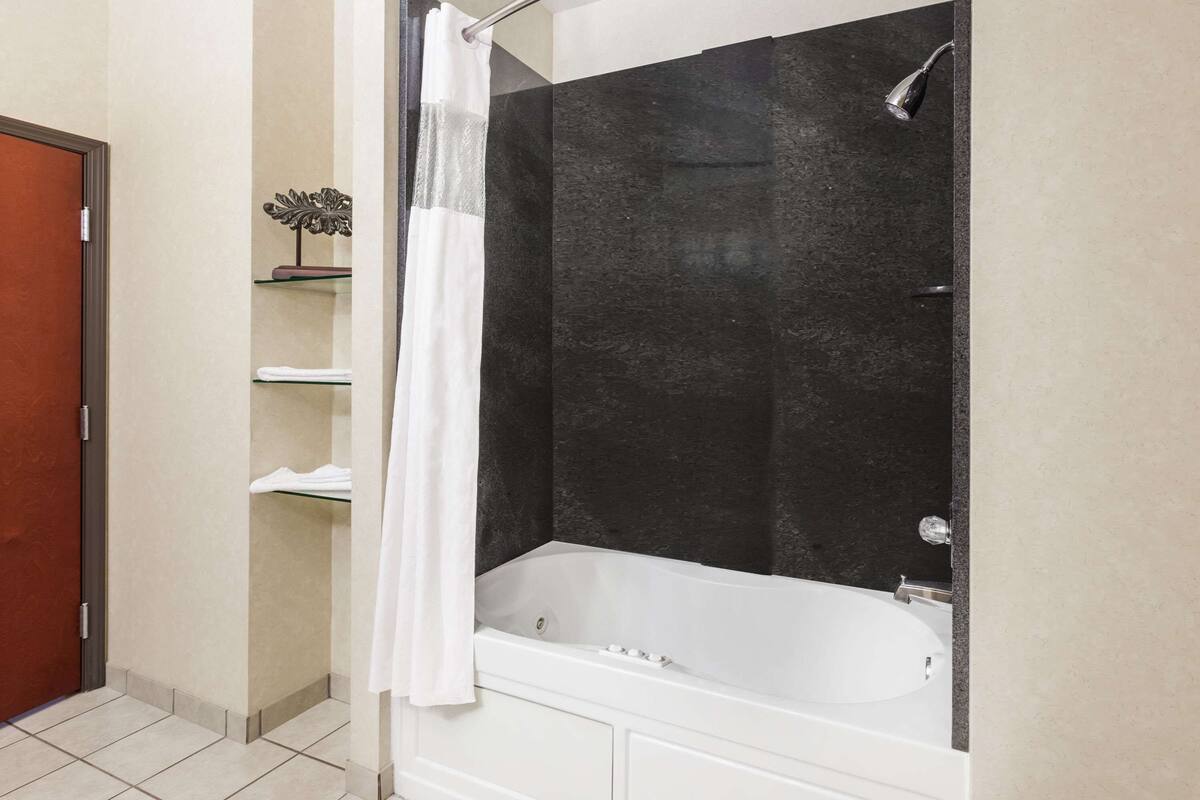 A bathroom with a bathtub, a shower curtain, and a shelf with towels.