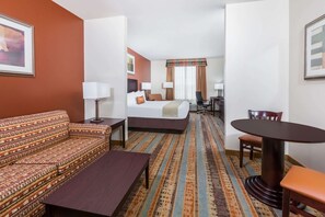 A hotel room with a sofa, a bed, a dining table, and a chair. - Baymont by Wyndham Henderson (Henderson)
