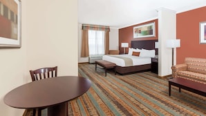 A hotel room with a bed, a desk, a chair, and a dining table. - Baymont by Wyndham Henderson (Henderson)