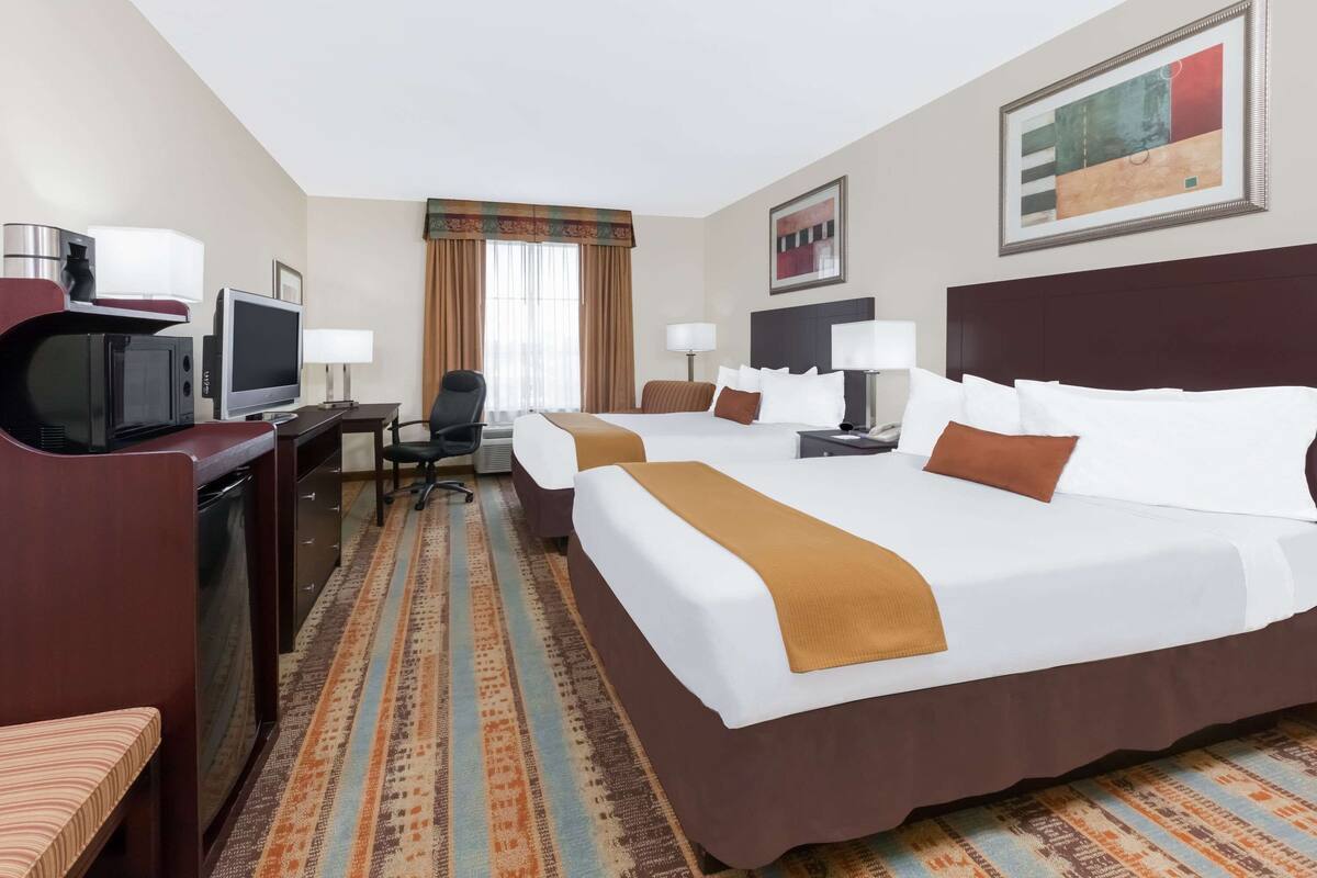 A hotel room with a large bed, a desk with a computer, a TV, and a microwave.