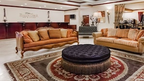 A lobby with two sofas and a round ottoman, a reception desk, and a large patterned rug. - Baymont by Wyndham Henderson (Henderson)