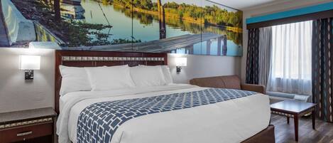 A hotel room with a large bed, a nightstand, a desk, and a view of a body of water through the window.