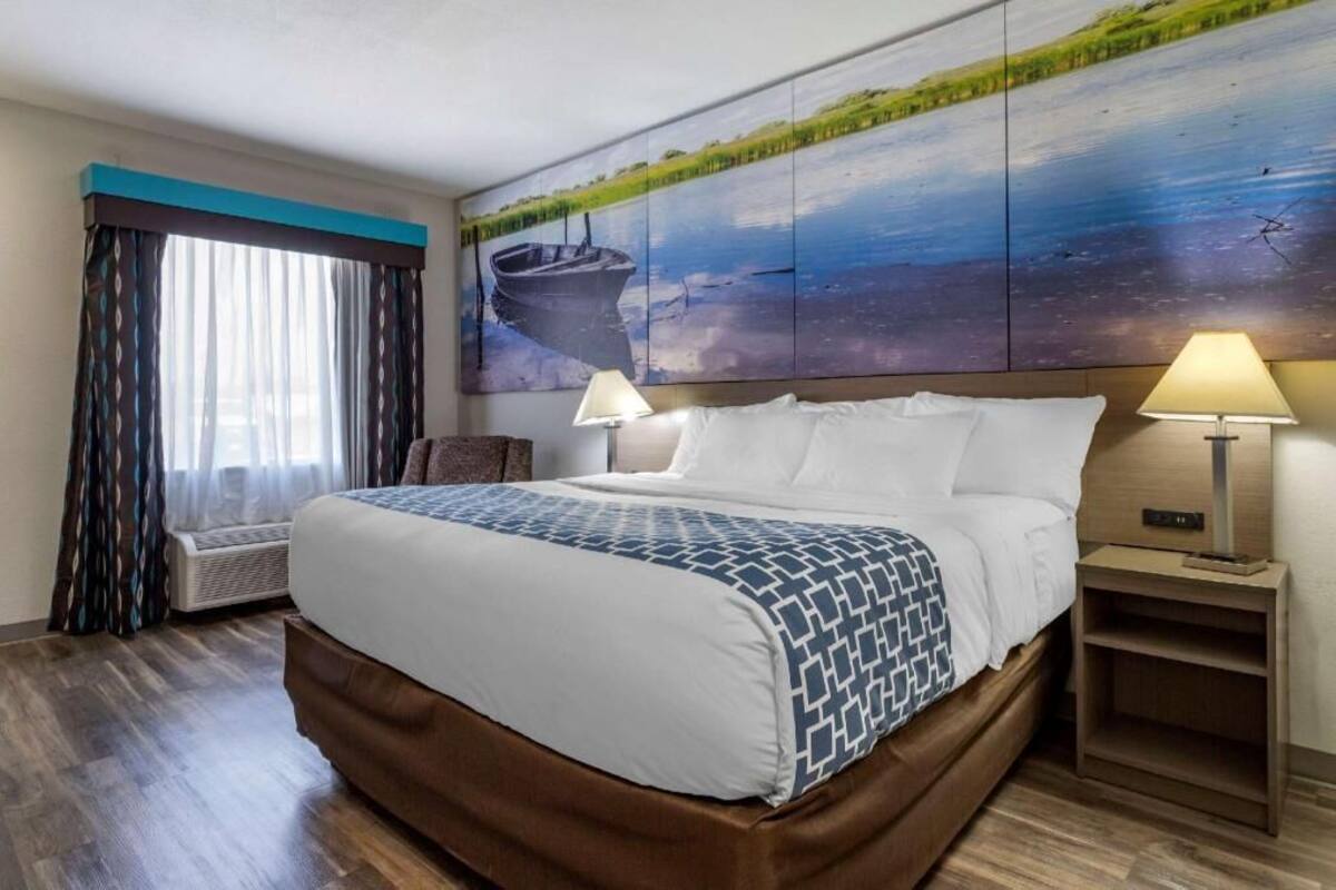 A hotel room with a large bed, two bedside lamps, a window with curtains, and a wall painting.