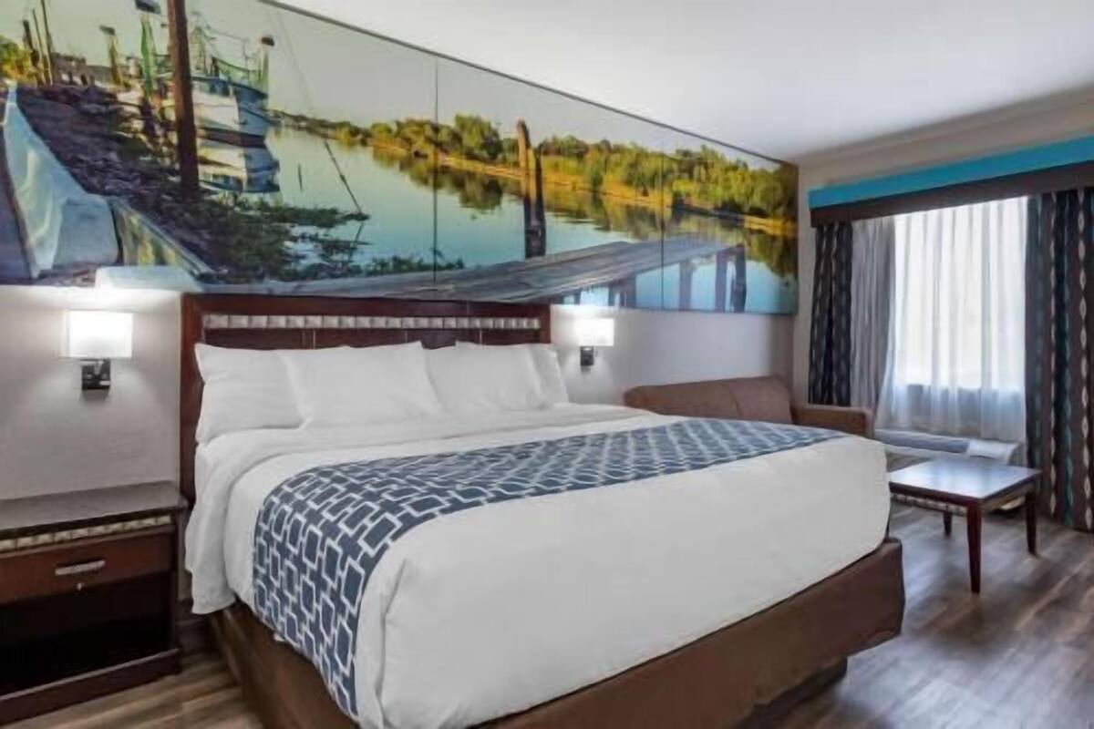 A hotel room with a large bed, a desk, a chair, a nightstand, and a painting on the wall.