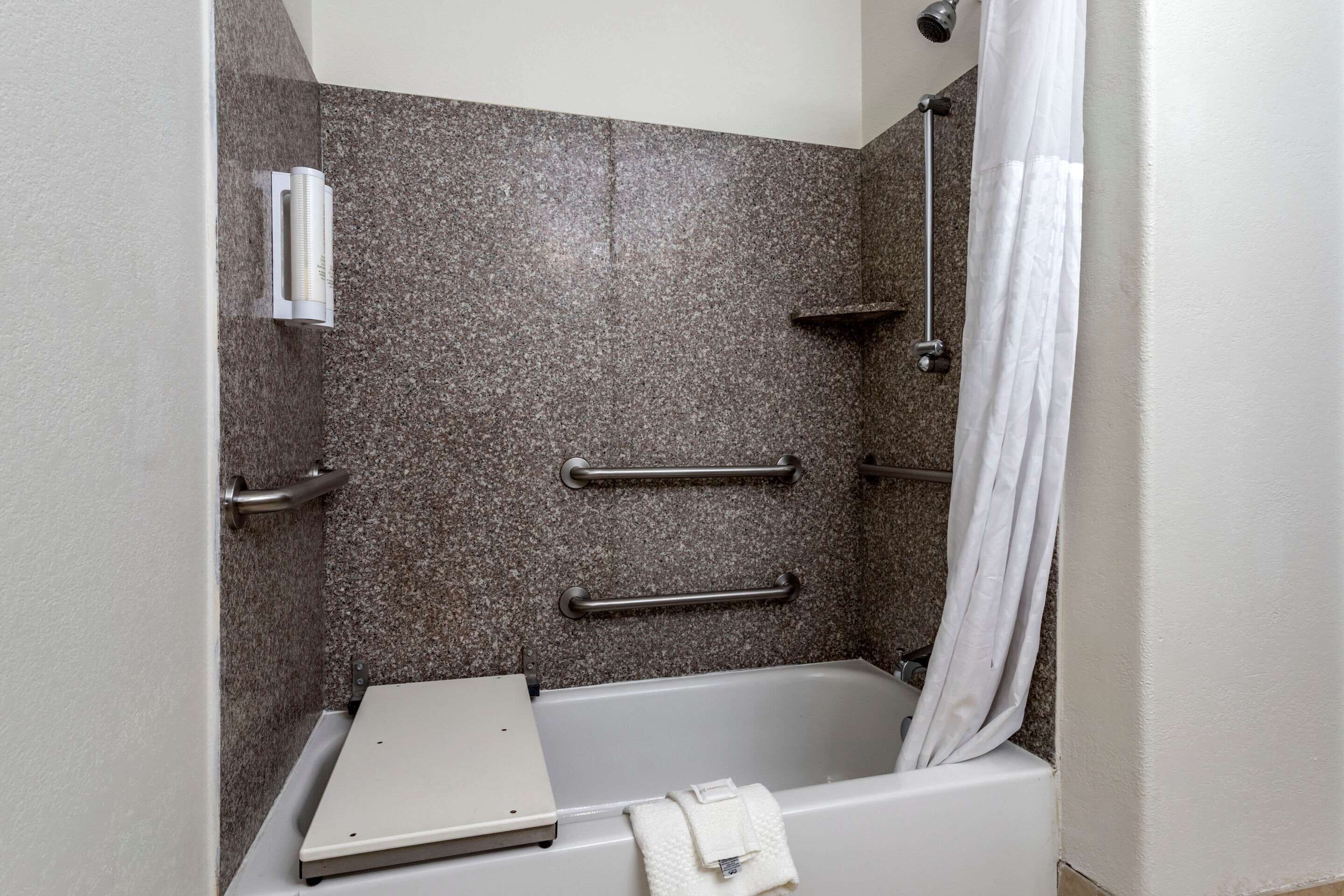 Un espace douche équipé d’une baignoire, de barres d’appui et d’un porte-serviettes.