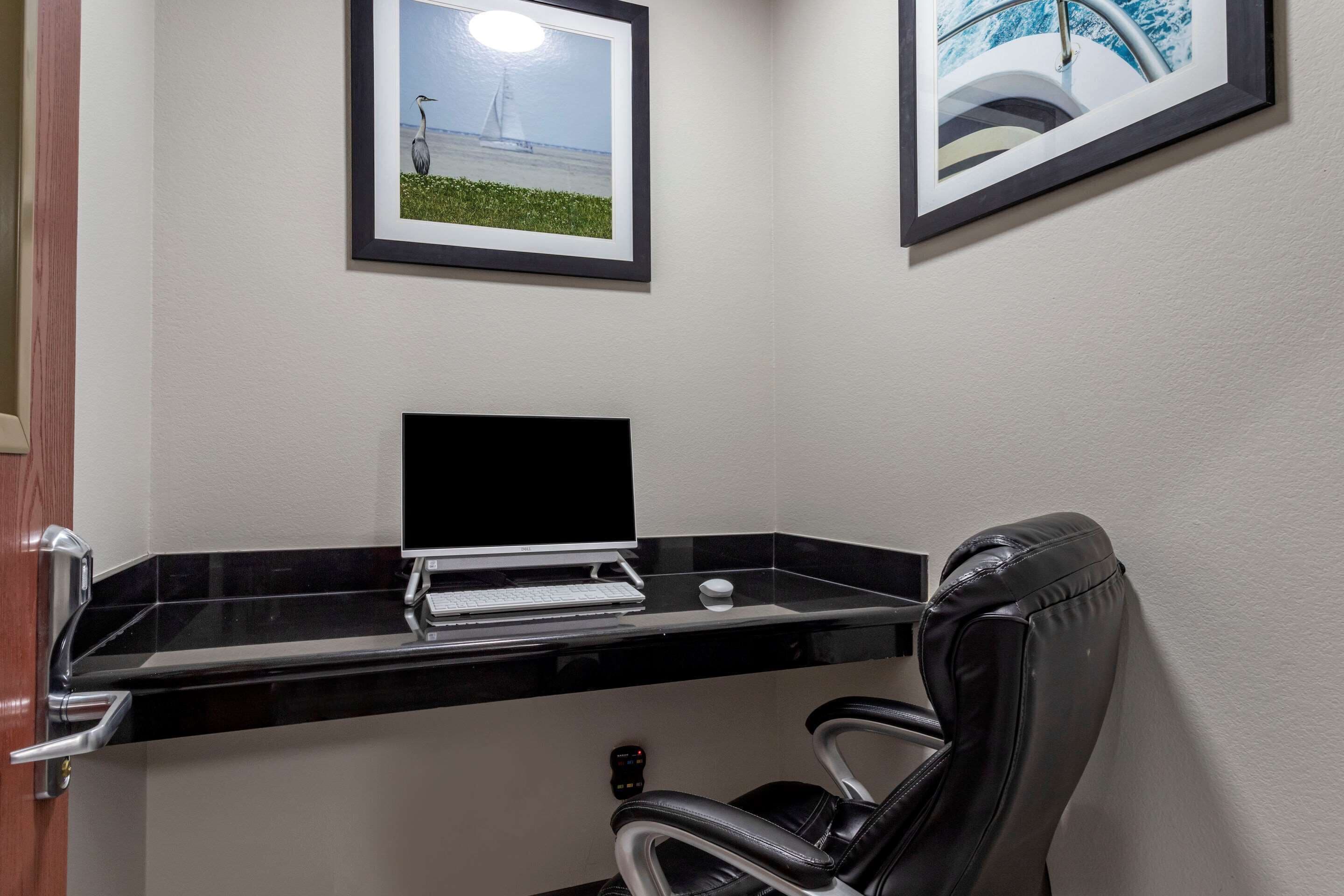 A corner office with a black desk, a laptop, a framed picture of a sailboat, and a black leather chair.