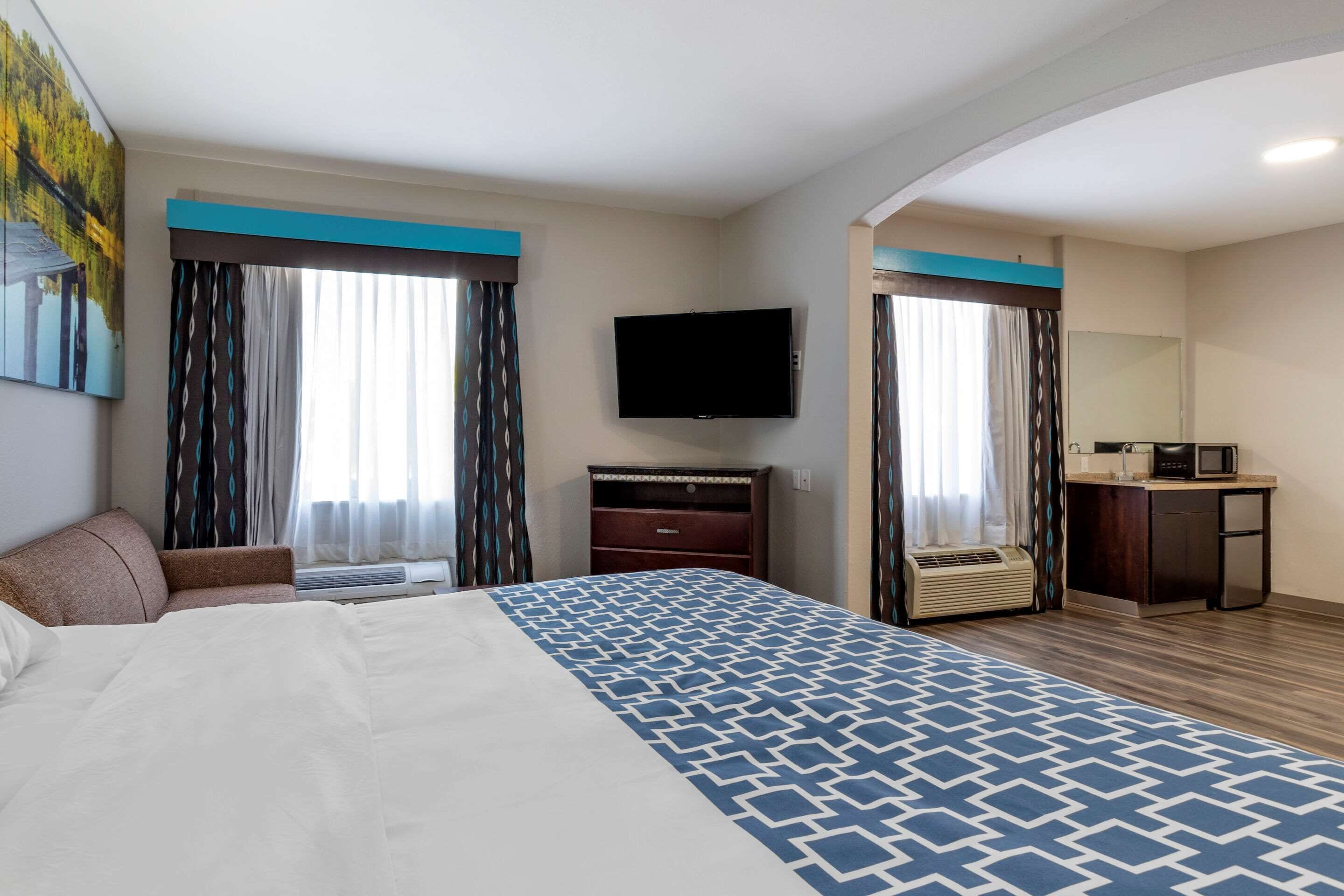 Habitación de hotel con una cama grande, un televisor de pantalla plana, un escritorio con microondas y un baño visible a través de una puerta abierta.