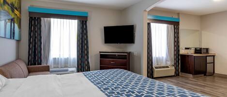Habitación de hotel con una cama grande, un televisor de pantalla plana, un escritorio con microondas y un baño visible a través de una puerta abierta.