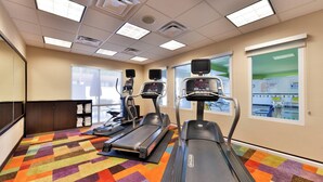 Une salle de sport équipée de tapis de course, de vélos elliptiques et d’une moquette aux couleurs vives.