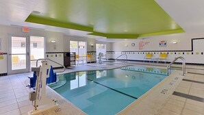 Une piscine intérieure à l’eau claire, avec des chaises longues jaunes et blanches, et un poste de surveillance pour le sauveteur.