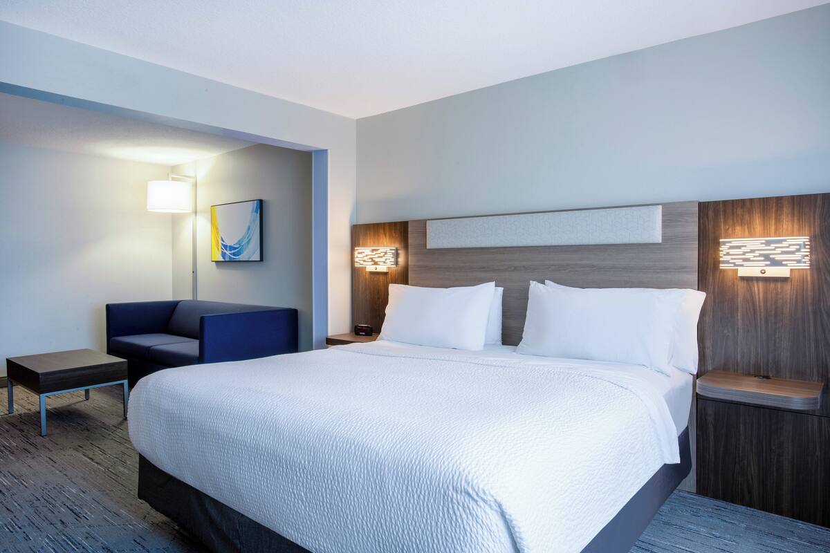 Hotellihuone, jossa on suuri sänky, työpöytä, tuoli ja kaksi seinään kiinnitettyä lamppua.
