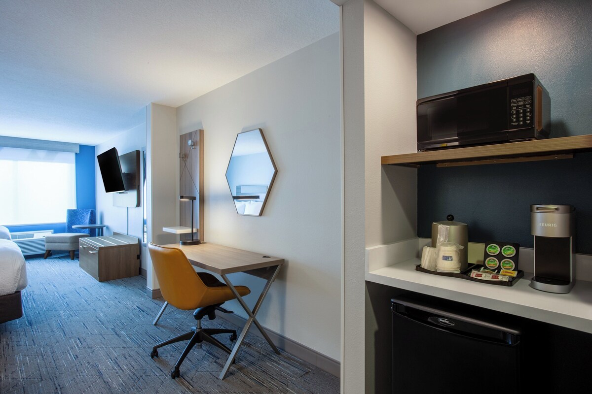 Habitación de hotel con cama, escritorio, silla, microondas, cafetera y lavavajillas.