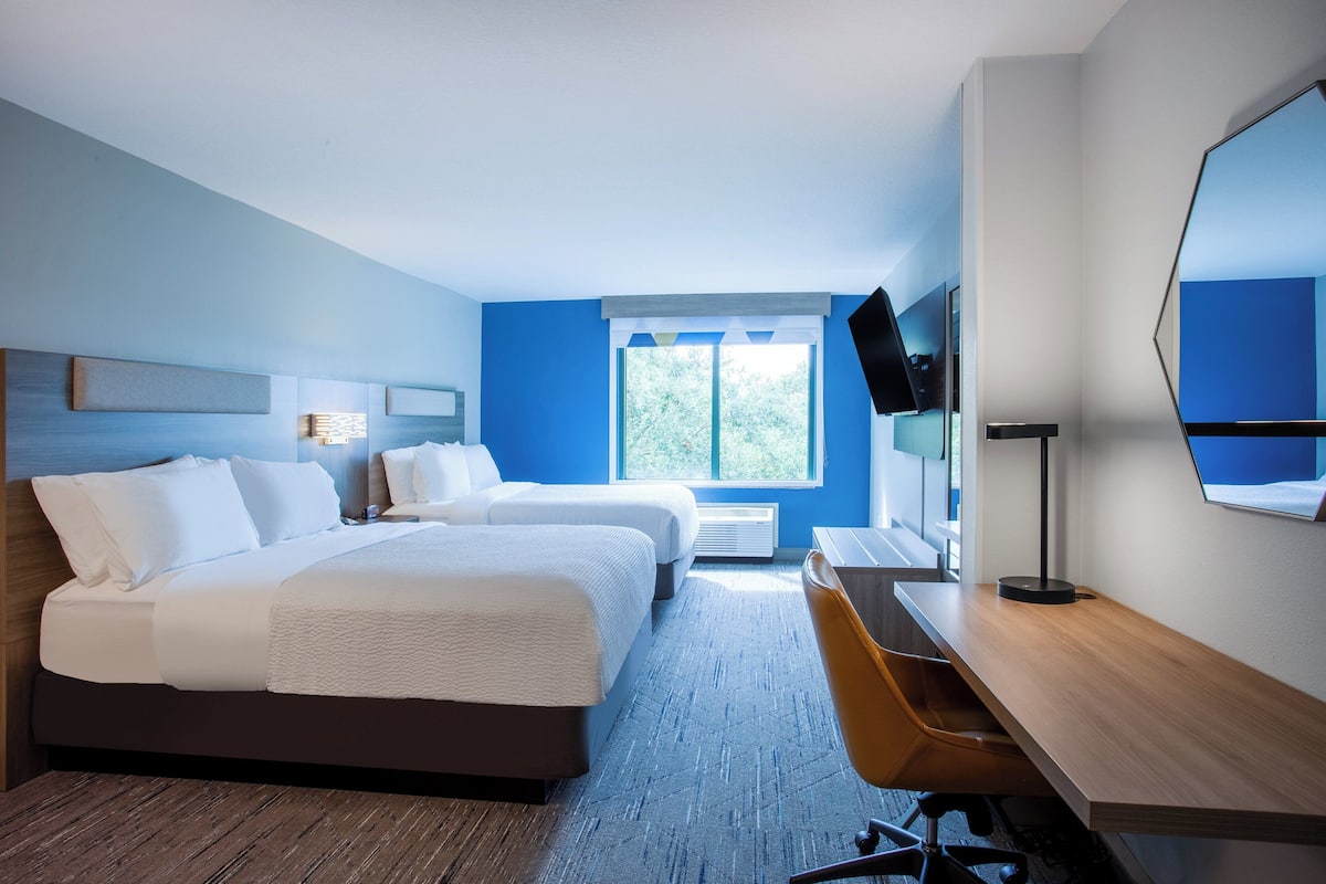 Hotellihuone, jossa on kaksi sänkyä, työpöytä, tuoli, televisio ja suuri peili.