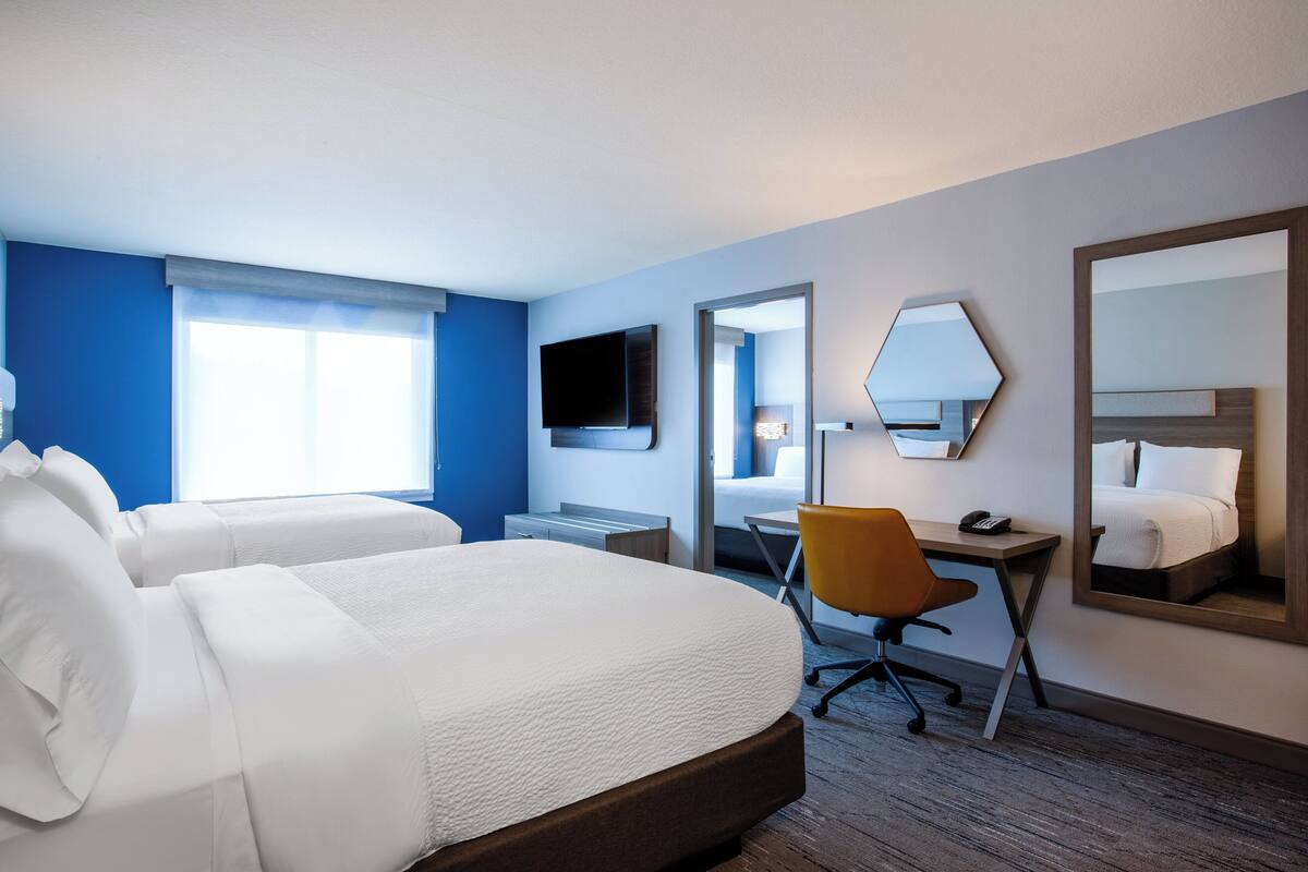 Hotellihuone, jossa on kaksi sänkyä, työpöytä, tuoli, televisio ja suuri peili.