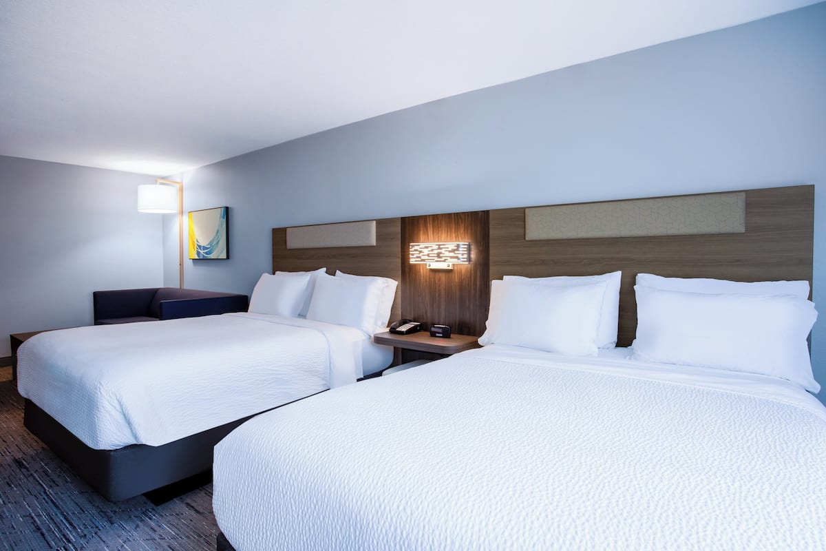 Hotellihuone, jossa on kaksi sänkyä, yöpöytä, jossa on puhelin ja lamppu, sekä seinään kiinnitetty valaisin.