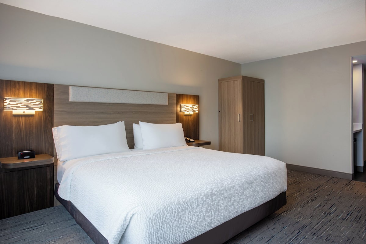 Moderni hotellihuone, jossa on suuri sänky, puinen pääty ja seinään kiinnitetyt valaisimet.