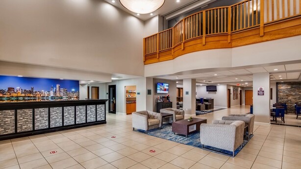 A hotel lobby with a cityscape mural, a reception desk, seating area, and a staircase to an upper level. - Best Western Plus Champaign/Urbana Inn (Champaign)