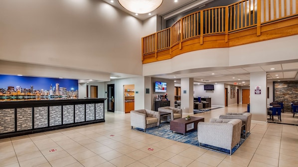 A hotel lobby with a cityscape mural, a reception desk, seating area, and a staircase to an upper level. - Best Western Plus Champaign/Urbana Inn (Champaign)