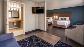 A hotel room with a bed, a TV, a bathroom with a mirror and sink, and a seating area with a table.
