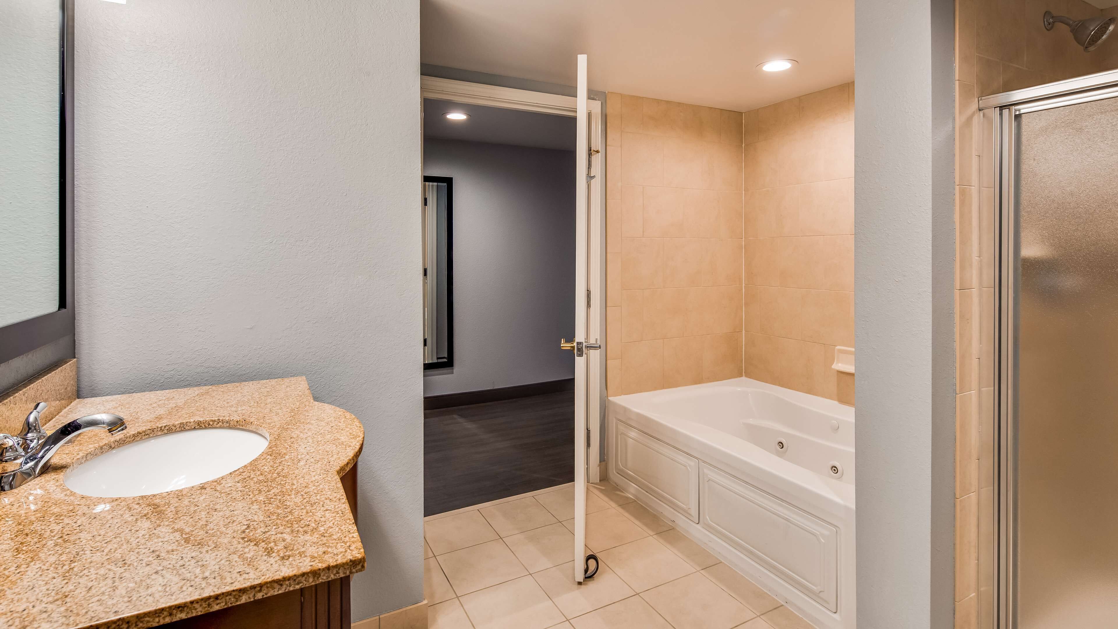 Une salle de bain avec un lavabo sur un plan de travail en granit, une baignoire et un espace douche.