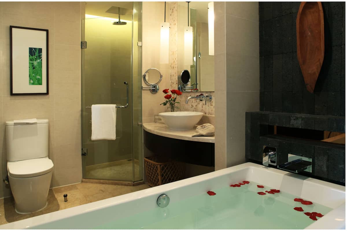 Une salle de bain dotée d’une douche à parois de verre, d’un lavabo blanc orné d’un vase de roses rouges et d’une baignoire parsemée de pétales de roses.