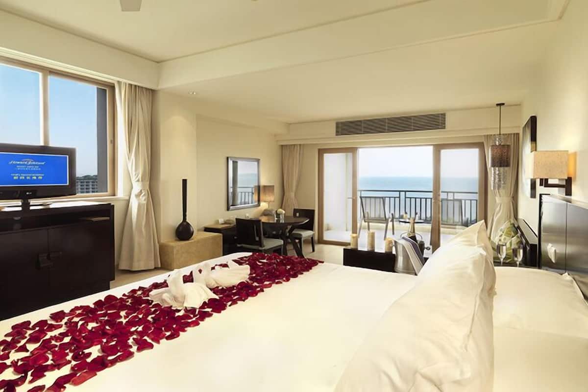 Une chambre d’hôtel équipée d’un lit, d’un bureau, d’une chaise, d’une télévision et d’un balcon avec vue sur la mer.