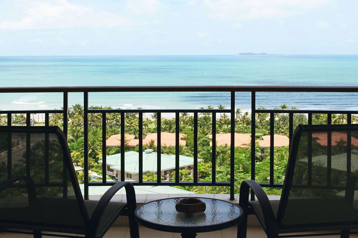 Un balcon avec deux chaises et une table, donnant sur une plage et l’océan.