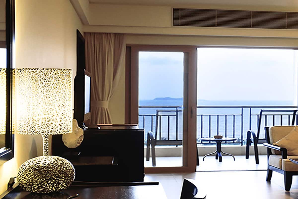 Une chambre d’hôtel avec un balcon, un canapé, une table basse et un fauteuil.