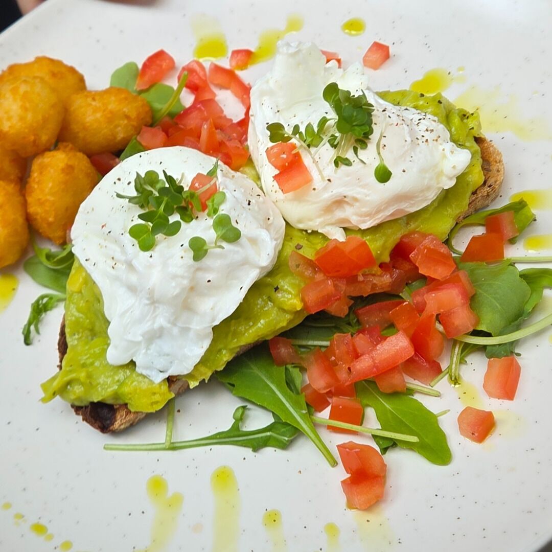 A plate with a green base topped with poached eggs, tomatoes, and greens, accompanied by golden-brown fried items.
