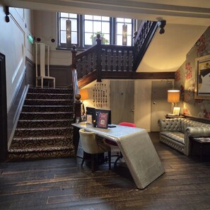 A grand staircase leading to a second floor, a cozy seating area with a sofa and armchairs, and a desk with a laptop and a framed picture. - Oddfellows Chester Hotel and Apartments (Chester)