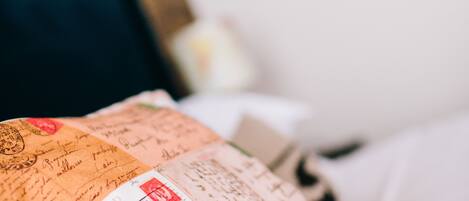 A bed with a white pillow and a blanket with a postal card design.