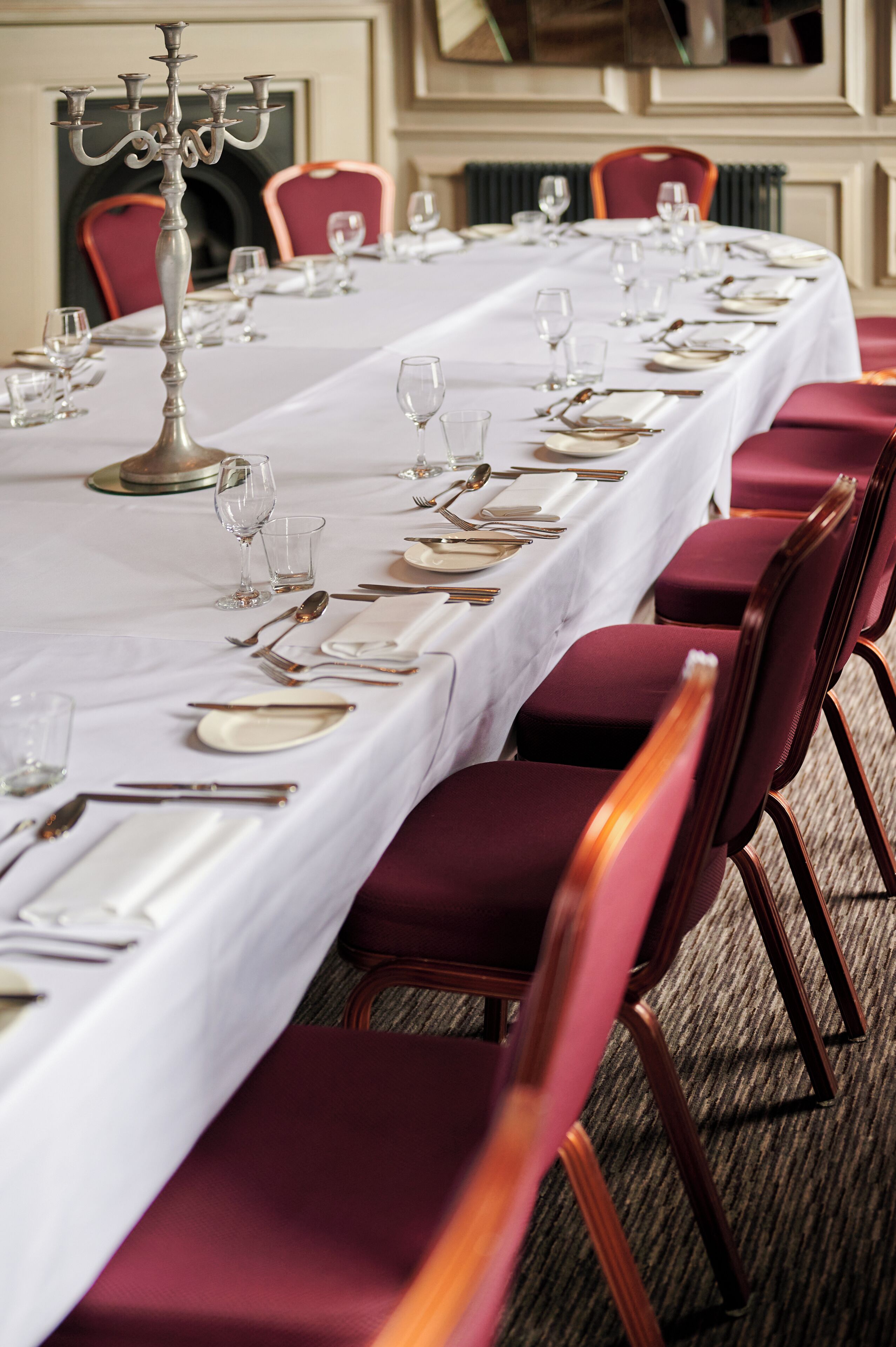 A long dining table set with white tablecloth, red chairs, and silverware.