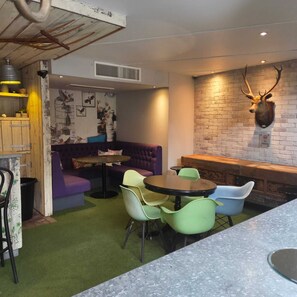 A cozy indoor seating area with a purple sofa, green and blue chairs, and a round table. A deer head mounted on a brick wall is visible. - Oddfellows Chester Hotel and Apartments (Chester)