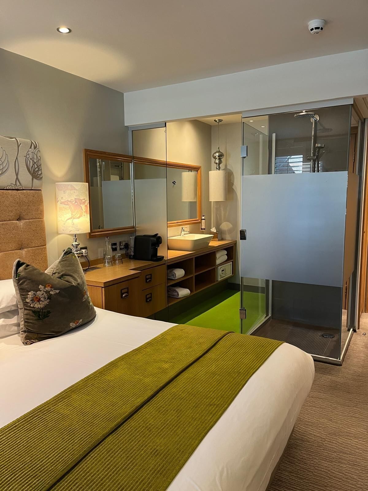 Ein Hotelzimmer mit Bett, Schreibtisch, Spiegel, Dusche und einem grünen Teppich.