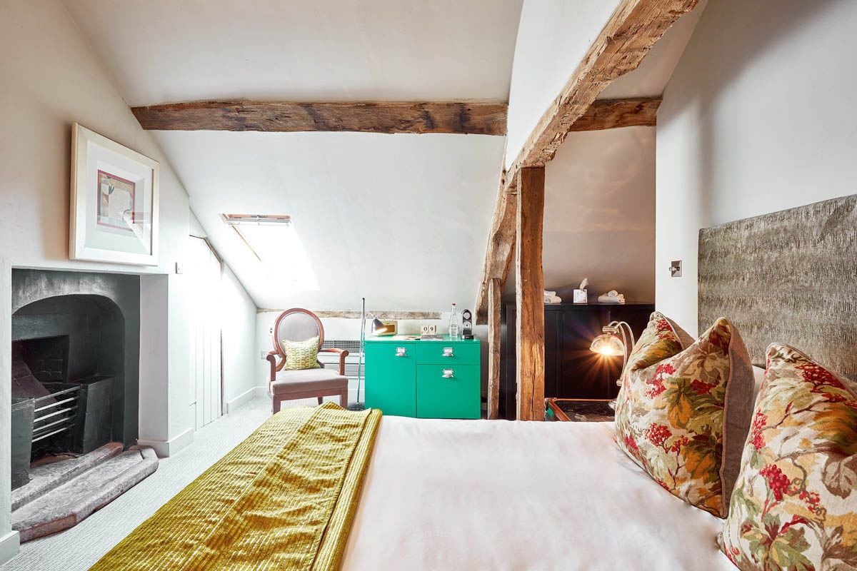 Ein Schlafzimmer mit einem Bett, einem grünen Schminktisch, einem Kamin und einem Holzbalken an der Decke.