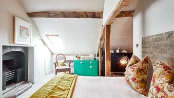 A bedroom with a bed, a green dresser, a fireplace, and a wooden ceiling beam.
