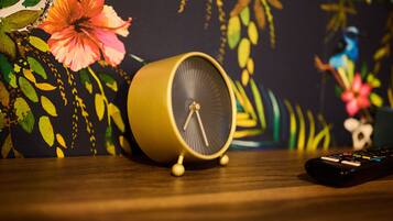 A yellow alarm clock on a wooden surface with a remote control beside it.