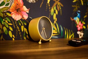 Un despertador amarillo sobre una superficie de madera, con un control remoto a su lado.