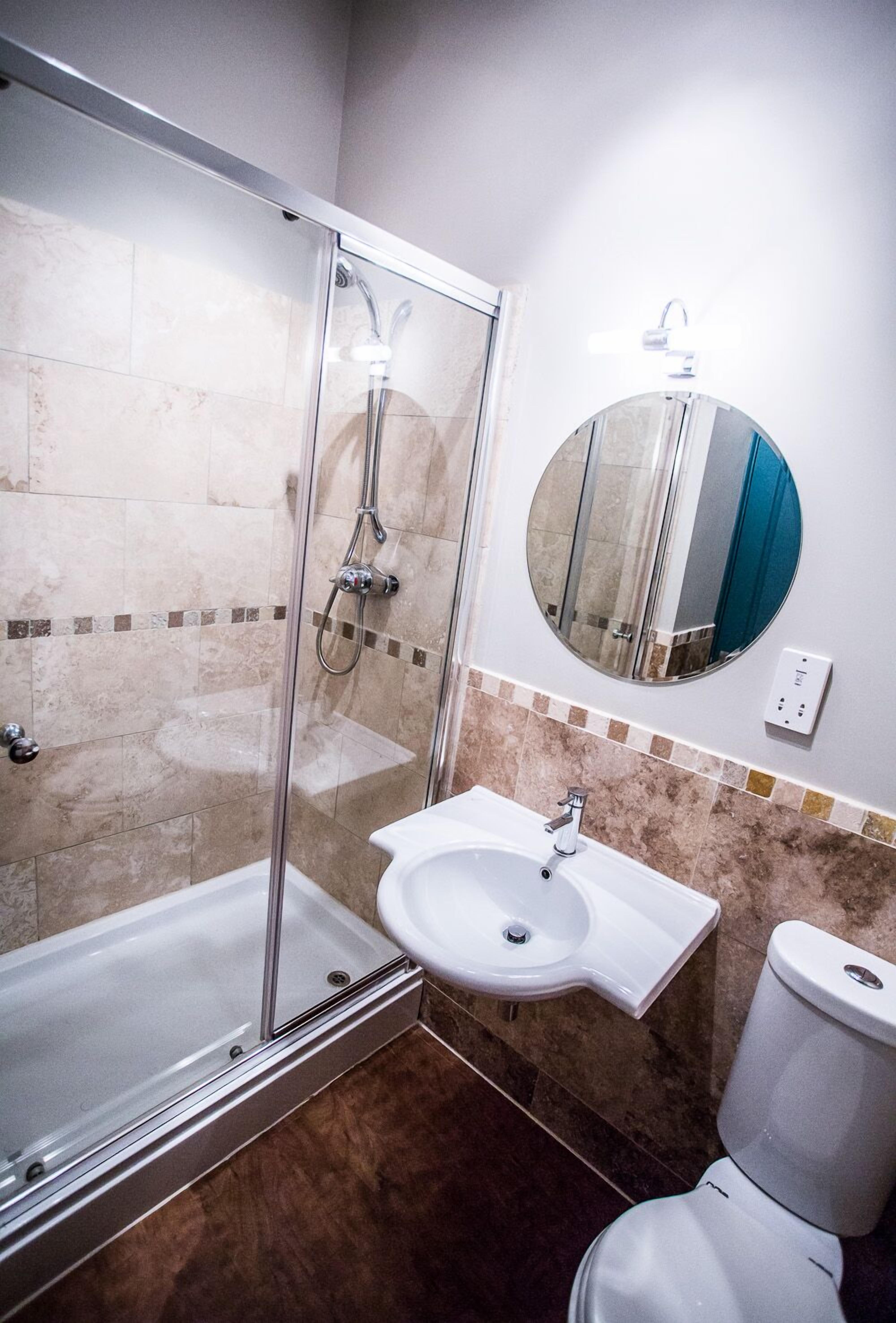 A bathroom with a glass-enclosed shower, a white sink, and a toilet.