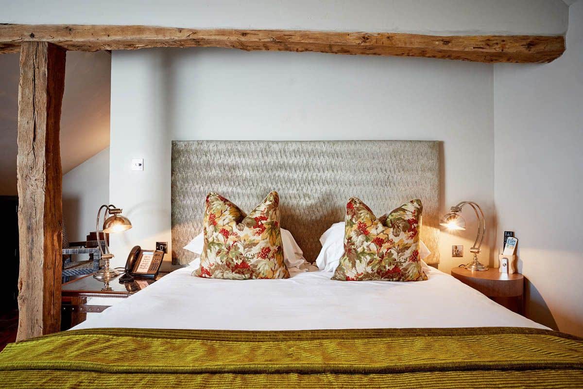 A bed with a wooden headboard, two floral pillows, a green bedspread, and bedside lamps.