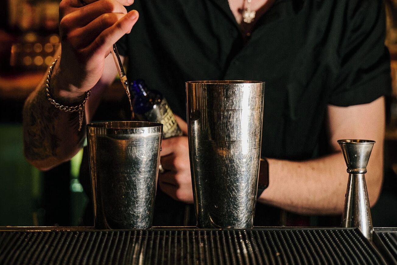 A bartender preparing drinks with a shaker and a tall glass on a bar counter.