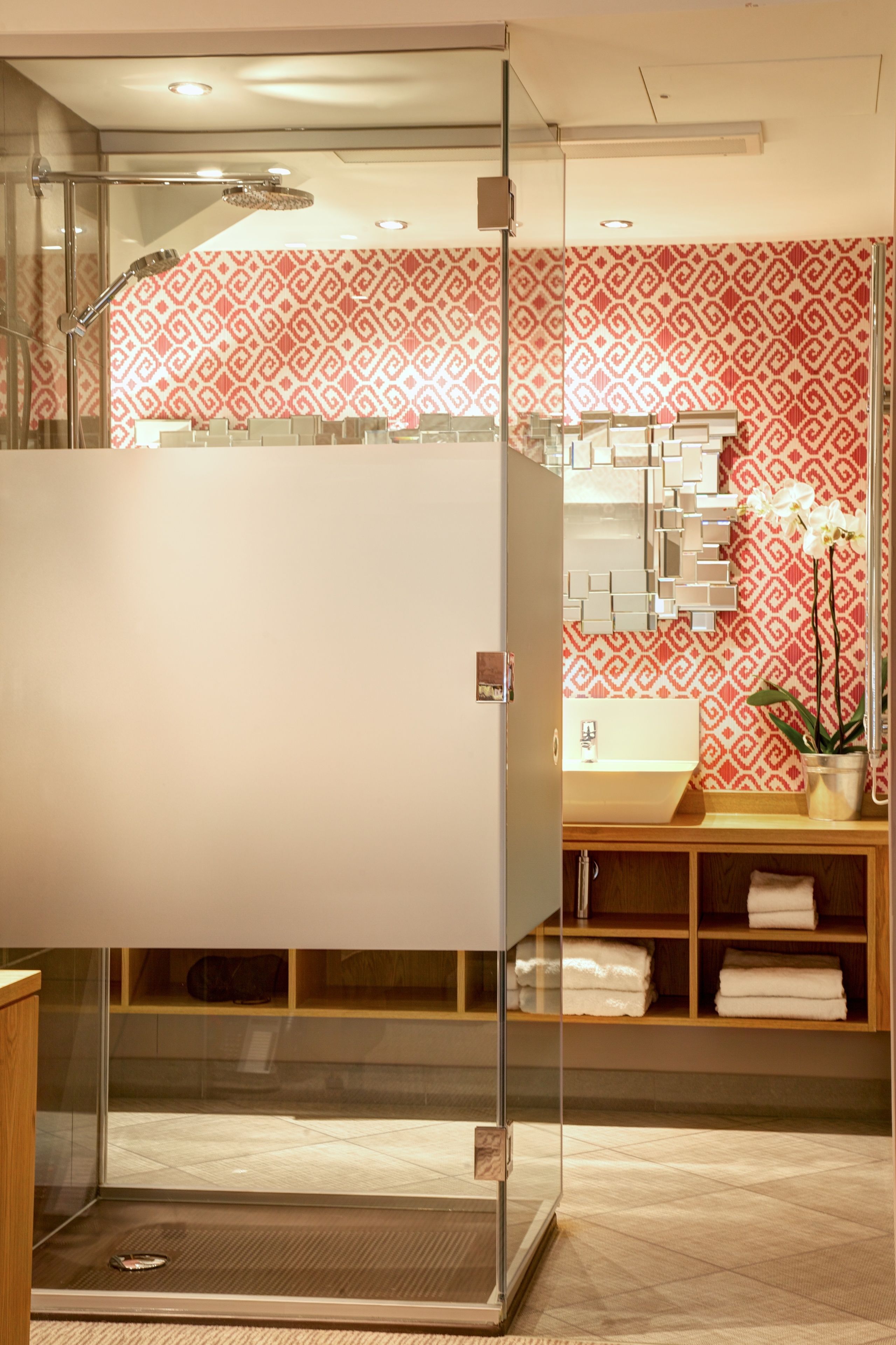 A modern bathroom with a glass shower enclosure, a sink with a patterned backsplash, and a wooden vanity with towels.