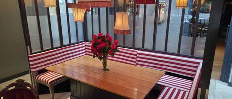 A dining area with a wooden table, red and white striped benches, and a vase of red roses.
