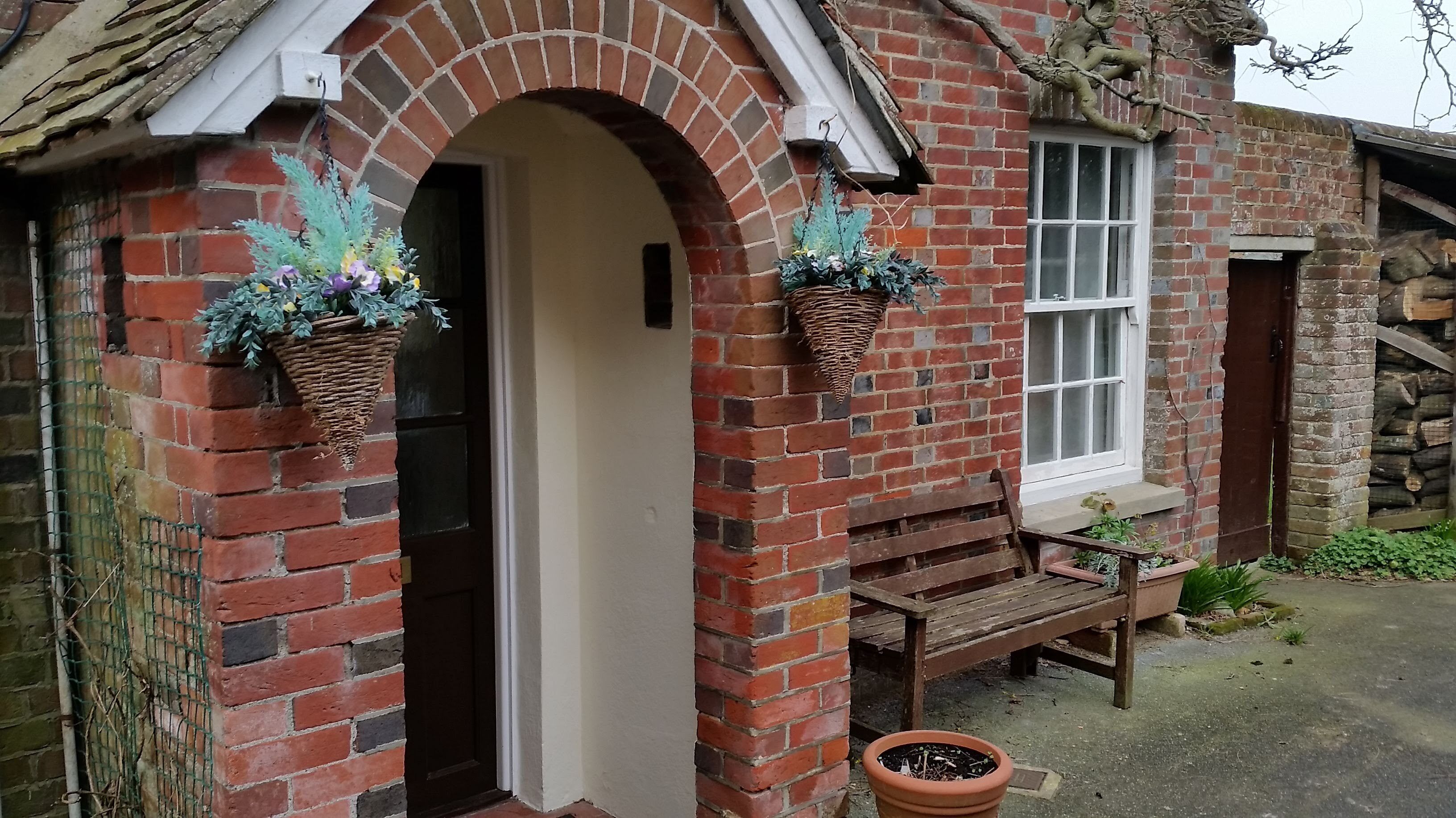 A brick house with a white door, a window, and a wooden bench outside.