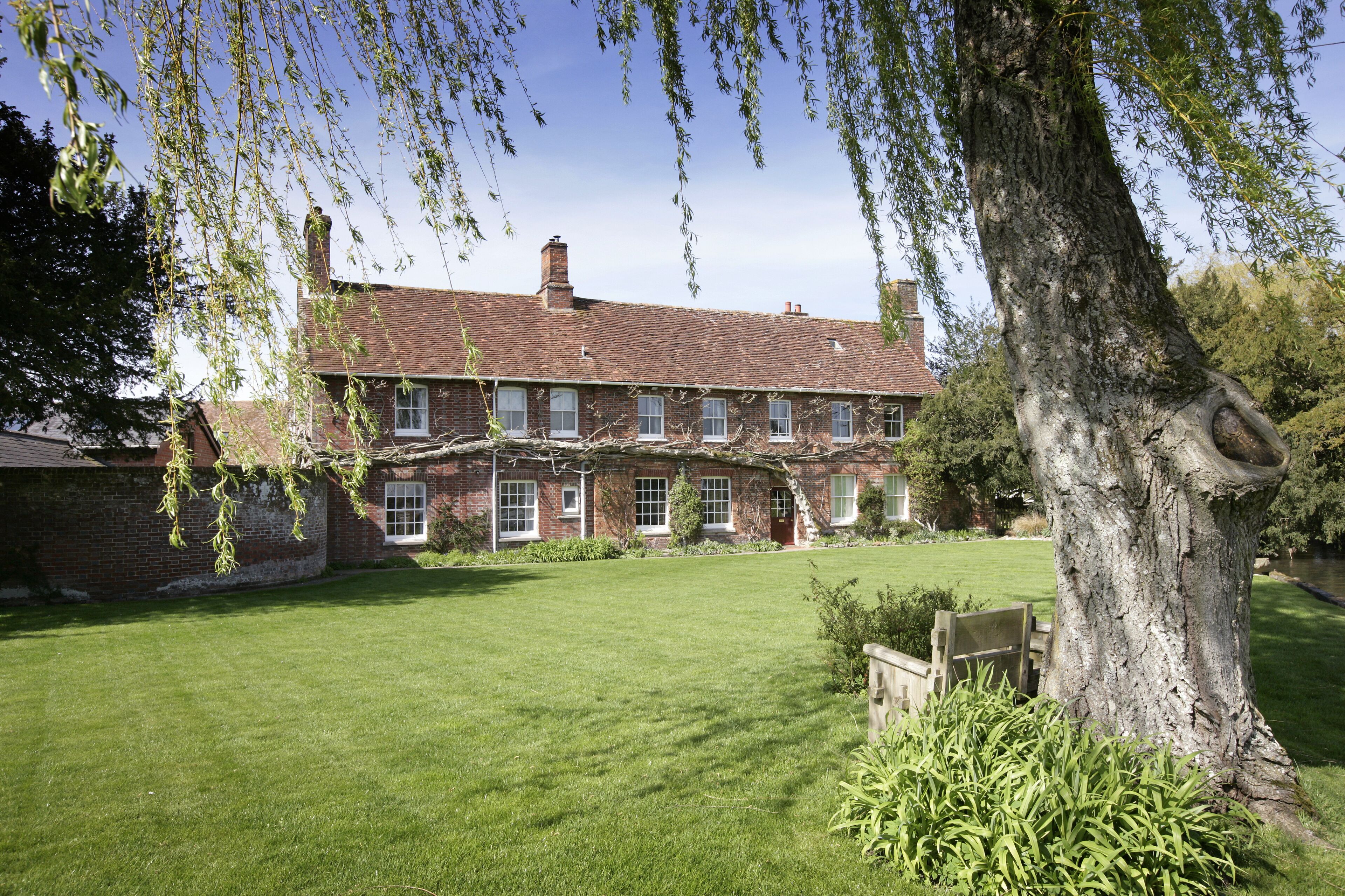 A traditional brick house with a well-maintained lawn and a large tree in the foreground.