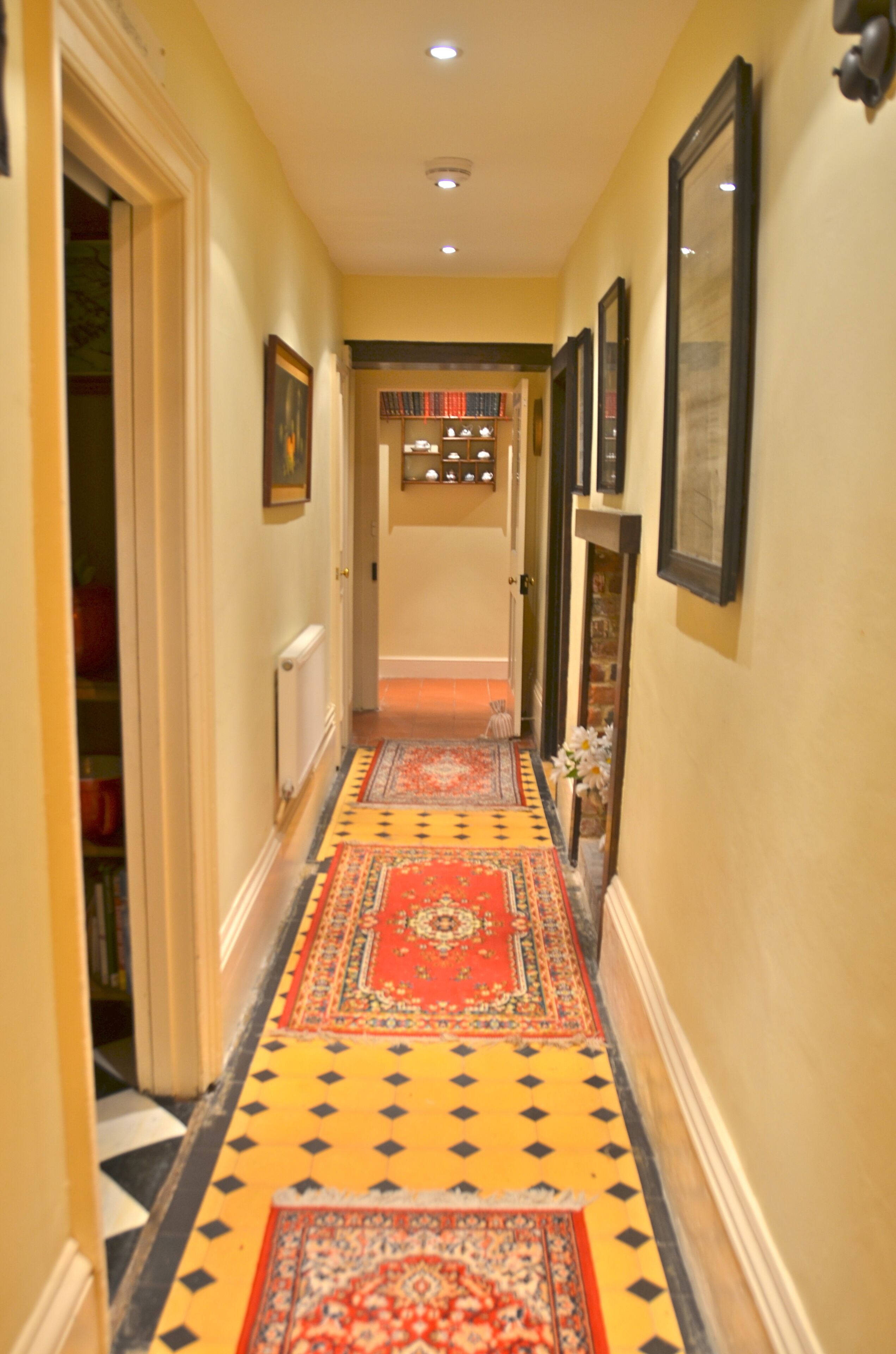 A hallway with patterned carpets, framed pictures on the walls, and a radiator on the left.