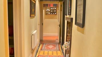 A hallway with patterned carpets, framed pictures on the walls, and a radiator on the left.